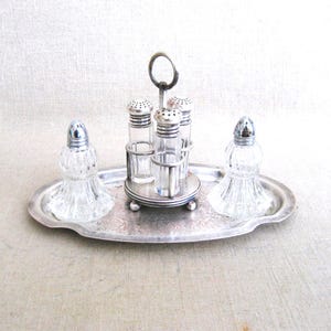 May include: A silver salt and pepper shaker set with four small glass shakers on a silver tray. The shakers have silver tops and are arranged in a circle on the tray.