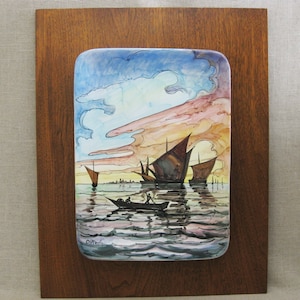 May include: A rectangular, framed artwork featuring a watercolor painting of boats on the water at sunset. The painting has a blue, orange, and brown color palette. The artwork is mounted on a dark brown wooden board.