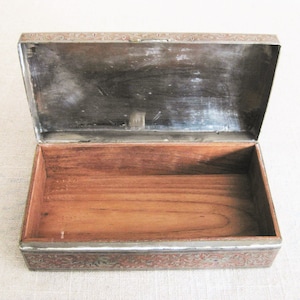 May include: An antique wooden box with a silver-colored lid. The lid is decorated with an intricate floral pattern. The box is open and the inside is lined with wood.
