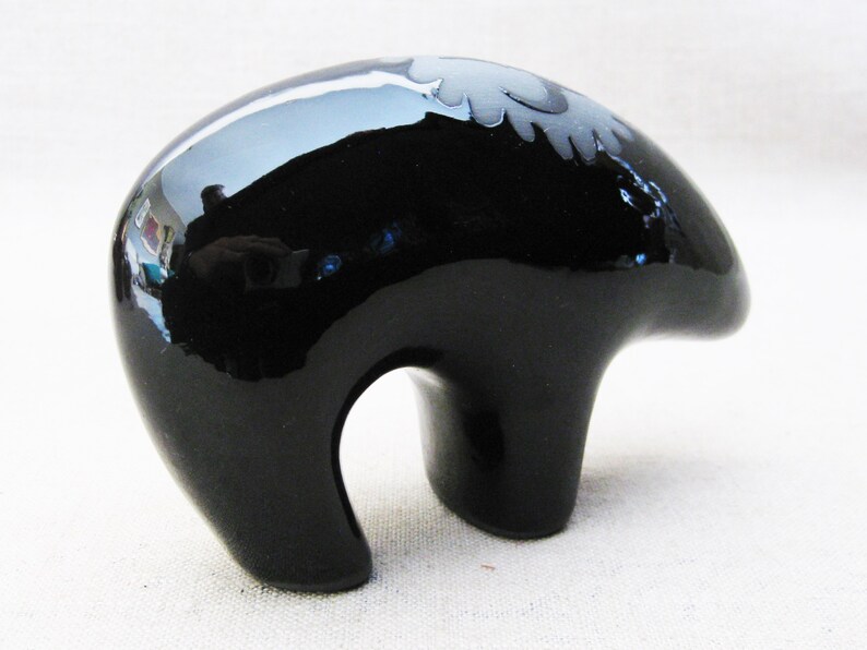 May include: A black ceramic bear figurine with a white design on its back. The bear is standing on all fours and has a glossy finish.