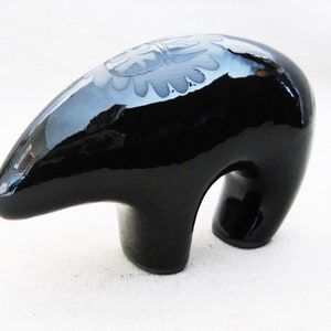 May include: A black ceramic bear figurine with a carved design on its back. The bear is standing on all fours and has a glossy finish.