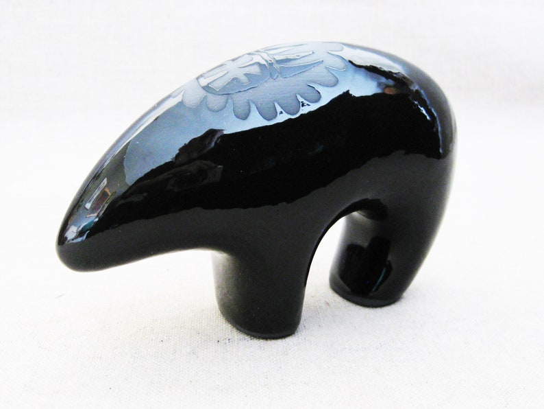 May include: A black ceramic bear figurine with a carved design on its back. The bear is standing on all fours and has a glossy finish.