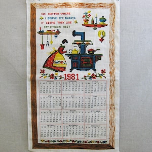 May include: A vintage 1981 kitchen towel with a calendar and a colorful embroidered image of a woman cooking on a wood-burning stove. The text reads "No matter where I serve my guests, it seems they like my kitchen best."