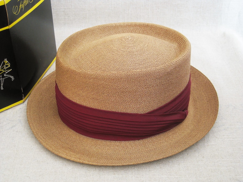 Pu&ograve; includere: Un cappello di paglia color beige con un'ampia tesa e un nastro bordeaux attorno alla corona.