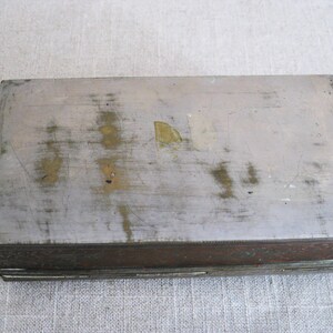 May include: A rectangular metal box with a worn, silver-colored top and a decorative, copper-colored bottom.