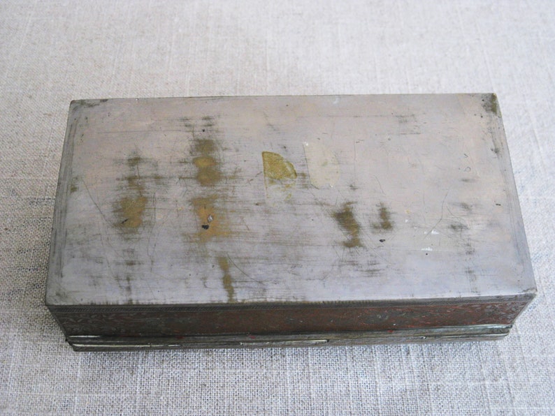 May include: A rectangular metal box with a worn, silver-colored top and a decorative, copper-colored bottom.