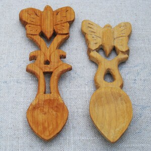 Peut inclure: Deux cuill&egrave;res en bois avec des sculptures de papillons. Les cuill&egrave;res sont en bois brun clair et ont une finition lisse. Les sculptures de papillons sont d&eacute;taill&eacute;es et complexes.