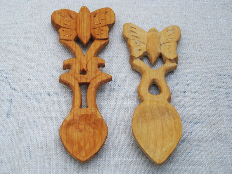 Peut inclure: Deux cuill&egrave;res en bois avec des sculptures de papillons. Les cuill&egrave;res sont en bois brun clair et ont une finition lisse. Les sculptures de papillons sont d&eacute;taill&eacute;es et complexes.
