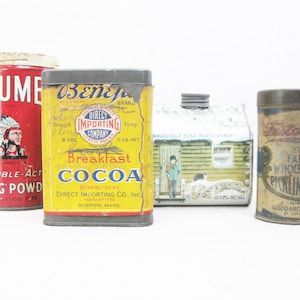 May include: Four vintage metal tins with various labels. The first tin is red with a Native American design and the text "Calume Double-Acting Baking Powder". The second tin is yellow with the text "Breakfast Cocoa" and "Direct Importing Co., Inc. Boston, Mass.". The third tin is green and white with the text "Absolutely Pure Maple Syrup". The fourth tin is brown with the text "225 Fancy Whole Mixed Pickling Spice Goddard Gro. Co. of  St. Louis, Mo."