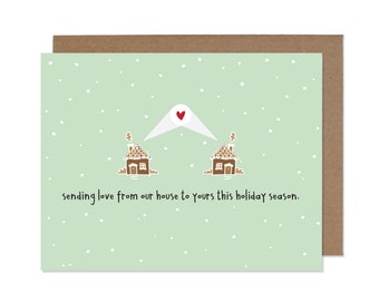 May include: A green holiday card with a white envelope with a red heart on it. The envelope is sending love from one gingerbread house to another gingerbread house. The text on the card reads "Sending love from our house to yours this holiday season."