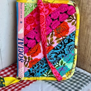 May include: A quilted fabric book cover with a vibrant patchwork design. The cover features a mix of floral and patterned fabrics in pink, red, orange, blue, and green. The spine has the word "SOCIAL" and the phrase "you are strong".