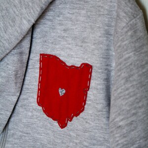 May include: Grey hooded sweatshirt with a red felt outline of the state of Ohio with a small white heart in the centre.