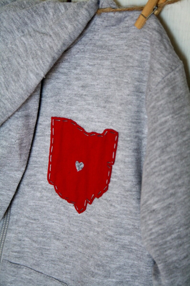 May include: Grey hooded sweatshirt with a red felt outline of the state of Ohio with a small white heart in the centre.