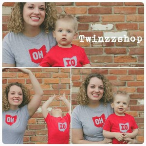 Pode incluir: Duas crian&ccedil;as vestindo camisas cinzas e vermelhas com o estado de Ohio e o estado de Iowa nelas. As crian&ccedil;as est&atilde;o em p&eacute; na frente de uma parede de tijolos. O texto "Twinzzshop" &eacute; vis&iacute;vel no canto superior direito da imagem.