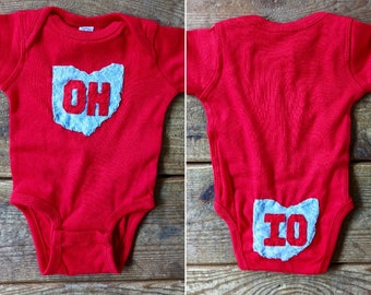 May include: Red baby onesie with a blue felt Ohio state outline on the front and back. The front says "OH" and the back says "IO".