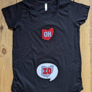 Pode incluir: Camiseta de maternidade preta com um contorno do estado de Ohio em vermelho e cinza e as letras "OH" na parte superior e um bal&atilde;o de fala branco com um contorno do estado de Ohio em cinza e vermelho e as letras "IO" na parte inferior.