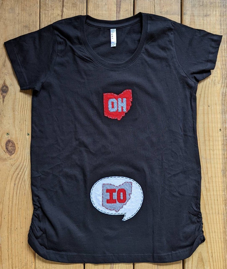Pode incluir: Camiseta de maternidade preta com um contorno do estado de Ohio em vermelho e cinza e as letras "OH" na parte superior e um bal&atilde;o de fala branco com um contorno do estado de Ohio em cinza e vermelho e as letras "IO" na parte inferior.