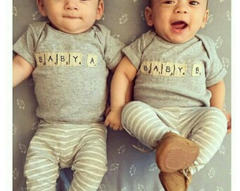 May include: Two babies wearing gray striped pants and gray shirts with the word "BABY" spelled out in letter tiles. The baby on the left has the word "BABY" spelled out with the letter "A" at the end. The baby on the right has the word "BABY" spelled out with the letter "B" at the end.
