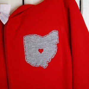 May include: Red hooded sweatshirt with a grey felt appliqu&eacute; of the state of Ohio with a red heart in the centre.