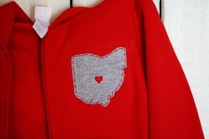 May include: Red hooded sweatshirt with a grey felt appliqu&eacute; of the state of Ohio with a red heart in the centre.
