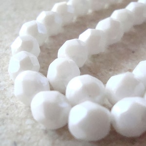 May include: A strand of white faceted glass beads. The beads are round and have a smooth, polished finish.