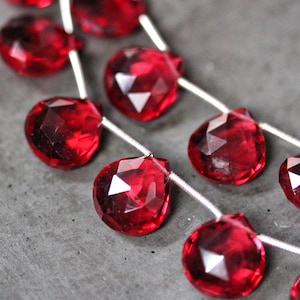 Può includere: Una collana di perle di pietra preziosa rossa sfaccettate infilate su un filo d'argento. Le perle sono a forma di goccia e hanno un'alta lucidatura.