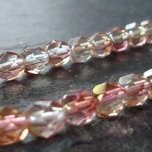 May include: A strand of iridescent glass beads in shades of pink, peach, and gold. The beads are faceted and have a shimmery finish.