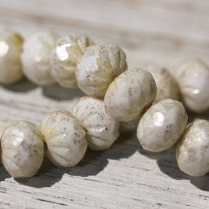May include: A strand of white glass beads with a textured, faceted surface. The beads have a subtle shimmer and are strung together on a clear thread.