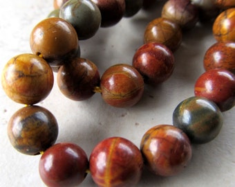 May include: A strand of brown, red, and gray gemstone beads. The beads are round and have a polished finish.
