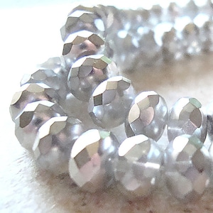 May include: A close-up of a strand of iridescent white faceted beads. The beads are round and have a smooth, polished finish.
