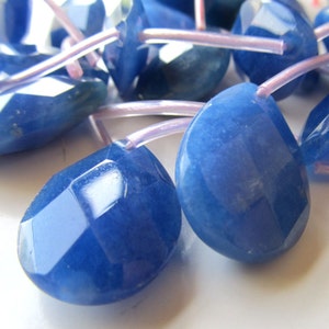 May include: A strand of blue gemstone beads with faceted surfaces. The beads are strung on clear elastic cord.