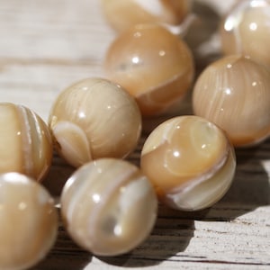 May include: A strand of beige and white iridescent shell beads. The beads are round and have a smooth, polished finish.