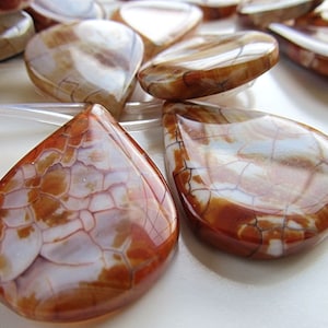 May include: A collection of teardrop-shaped agate beads with a white and brown marbled pattern. The beads have a smooth, polished finish.