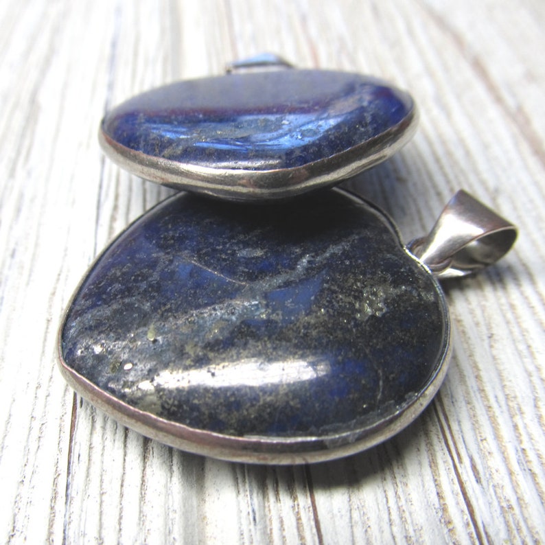 Puede incluir: Dos colgantes en forma de coraz&oacute;n hechos de piedra lapisl&aacute;zuli azul oscuro con engastes de plata.
