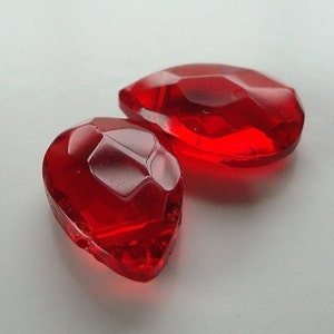 May include: Two red glass teardrop-shaped beads with faceted surfaces.