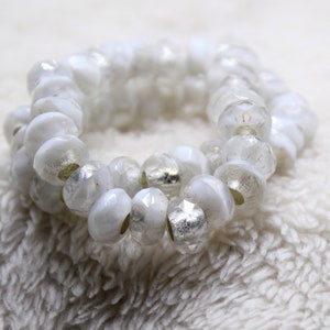 May include: A white beaded bracelet with silver accents. The beads are faceted and have a slightly iridescent finish.