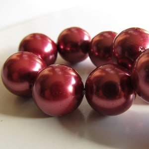 May include: A strand of maroon faux pearl beads. The beads are round and have a glossy finish.