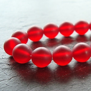 May include: A strand of red glass beads with a frosted finish. The beads are round and have a slight shine.