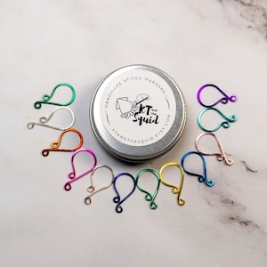 May include: A set of 10 colorful metal stitch markers in a small tin container. The tin is labeled "Handmade Stitch Markers KT Squid handmadesquid.etsy.com".