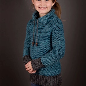 A young girl with a warm smile, dressed in a cozy blue crochet sweater.