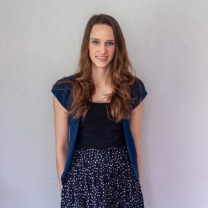 May include: A woman wearing a blue cardigan over a black top and a black and white polka dot skirt.