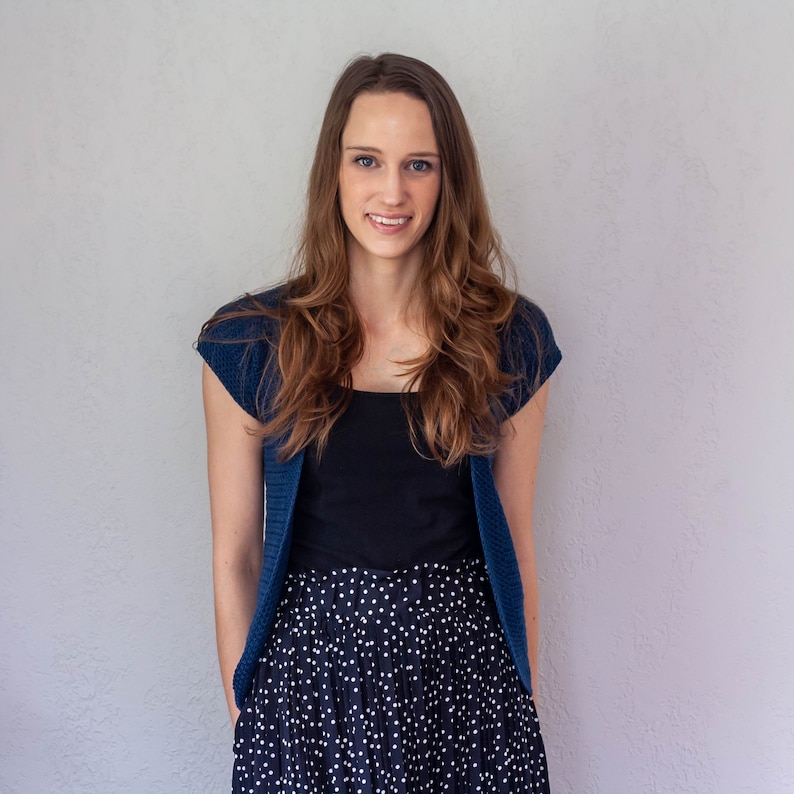May include: A woman wearing a blue cardigan over a black top and a black and white polka dot skirt.