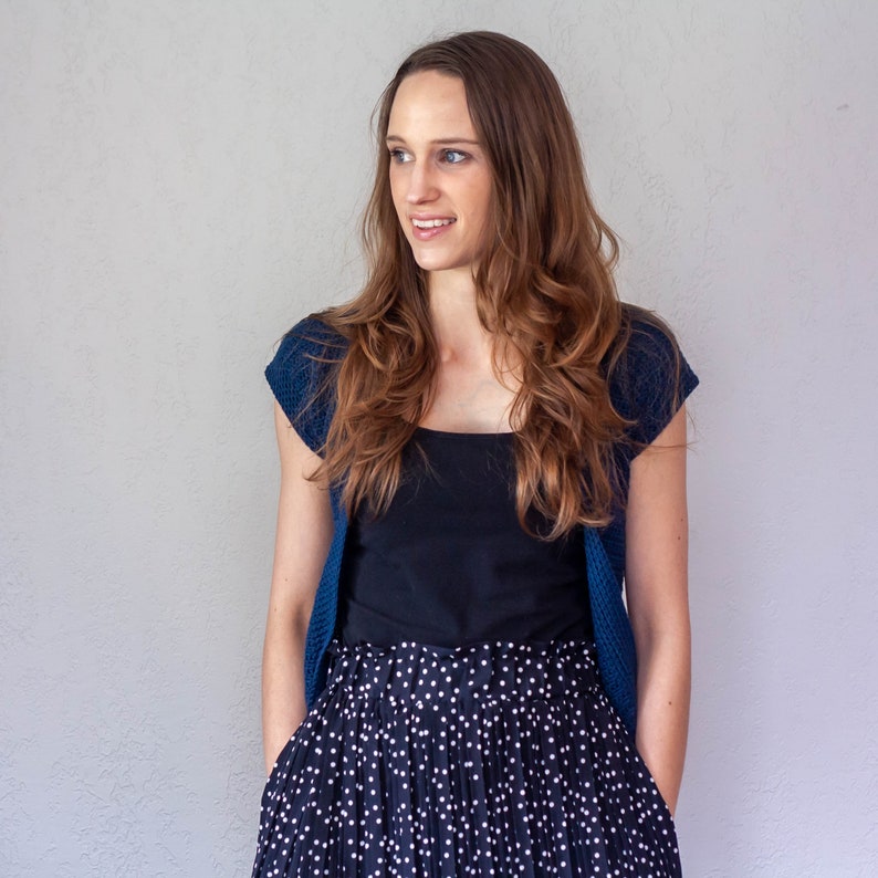 May include: A woman wearing a blue cardigan over a black tank top and a black and white polka dot skirt.