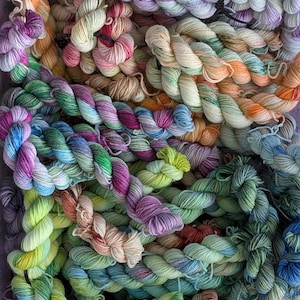 May include: A collection of hand-dyed yarn skeins in a variety of variegated colors including shades of green, purple, blue, orange, pink, and cream. The twisted yarn bundles are arranged in a dense pile, showcasing multi-colored fiber textures.