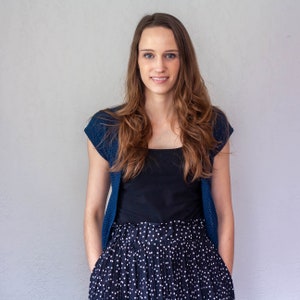 May include: A woman wearing a blue cardigan over a black top and a black and white polka dot skirt.