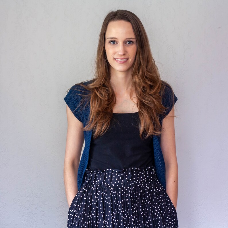 May include: A woman wearing a blue cardigan over a black top and a black and white polka dot skirt.