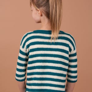 An adorable girl with a vibrant striped crochet sweater, showcasing her playful and fashionable side.