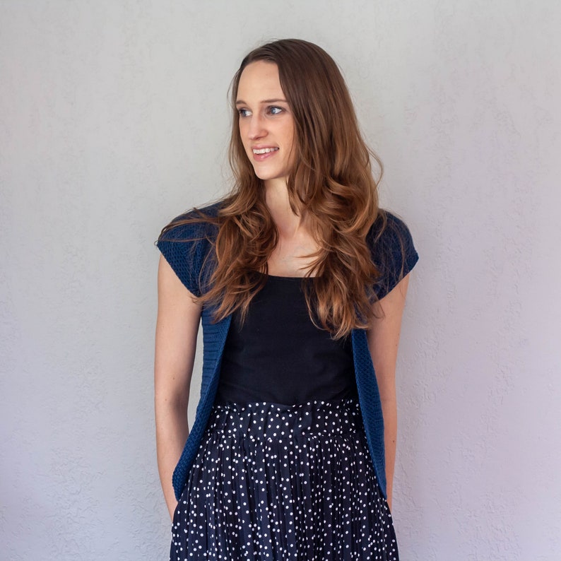 May include: A woman wearing a blue cardigan over a black tank top and a black and white polka dot skirt.
