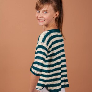 A cheerful young girl in a striped crochet sweater, radiating warmth and style.