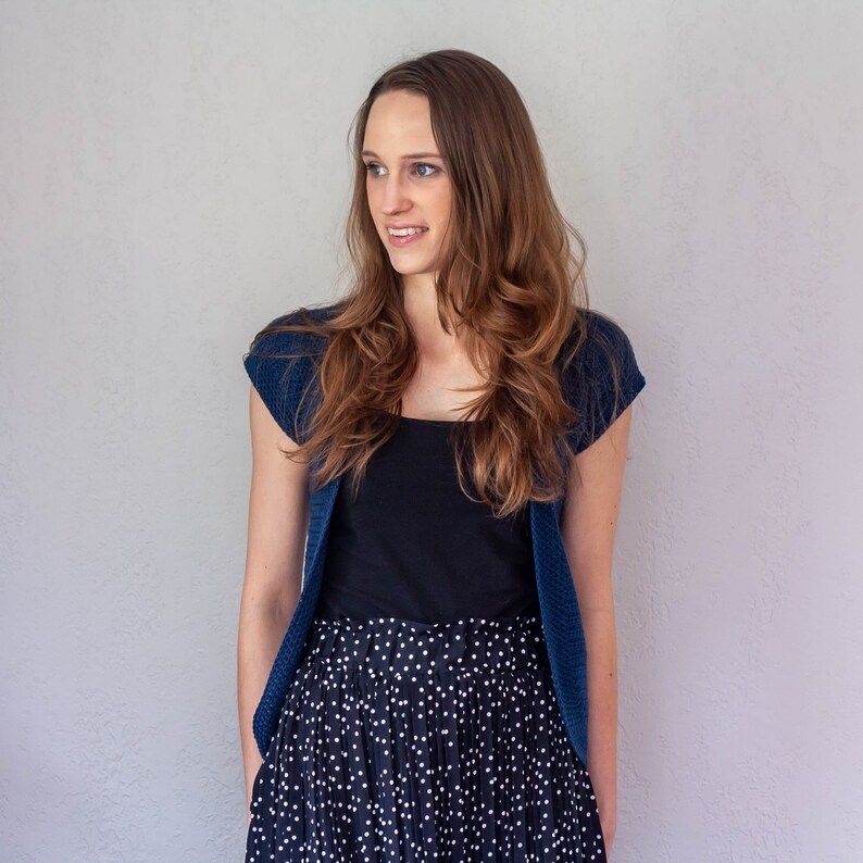 May include: A woman wearing a blue cardigan over a black top and a black and white polka dot skirt.